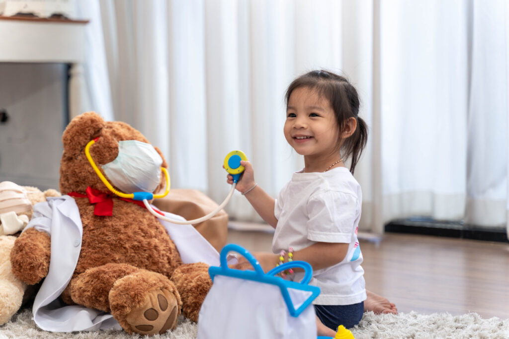A happy Asian girl playing doctor or nurse listening to a stethoscope to the toy.