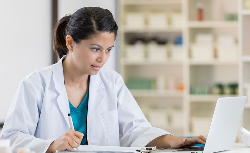 Doctor looking at laptop and writing in a notebook